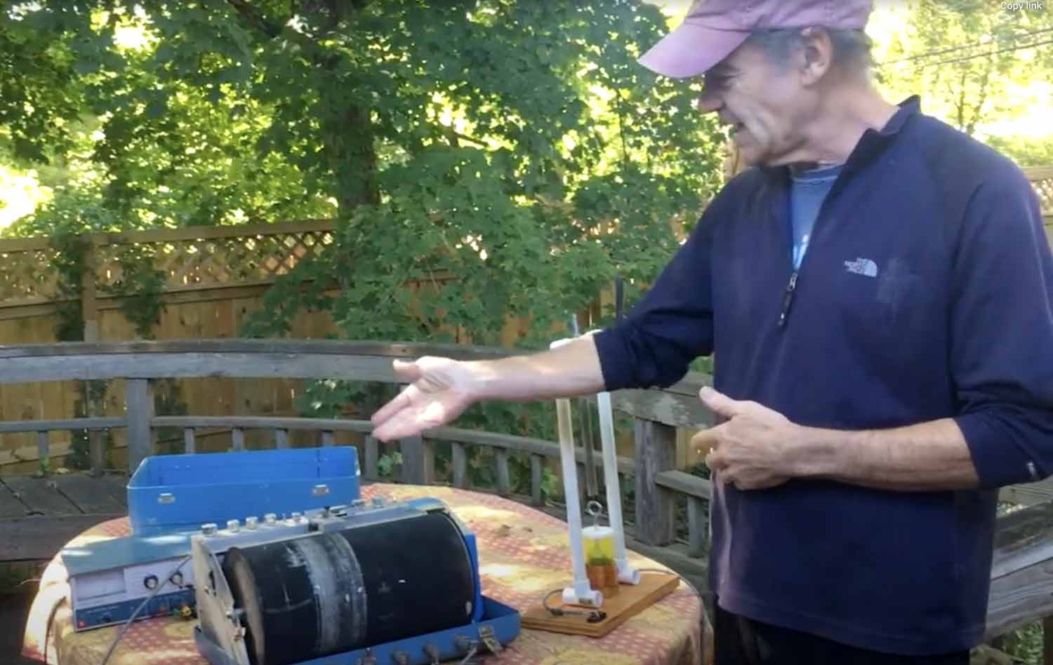 A man gesturing toward a piece of scientific equipment on a table.